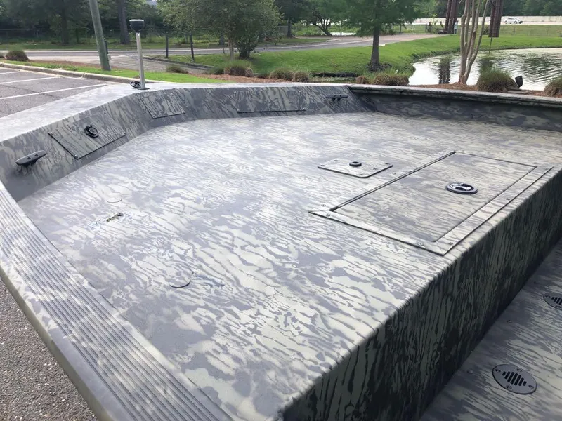 Slide: The Image of 2025 Tracker Grizzly 1860 CC boat with camo deck, parked near a pond. - 9