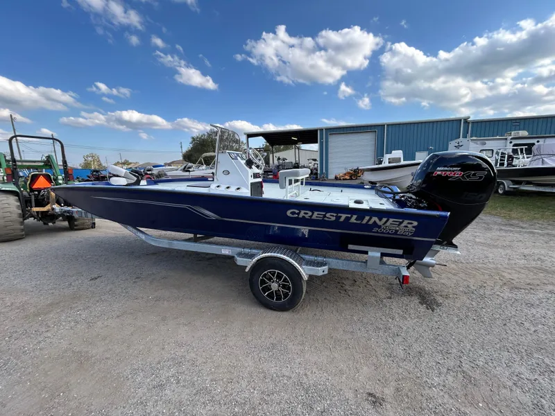 Slide: The Image of 2025 Crestliner 2000 Bay boat on trailer, parked outdoors under a partly cloudy sky. - 3