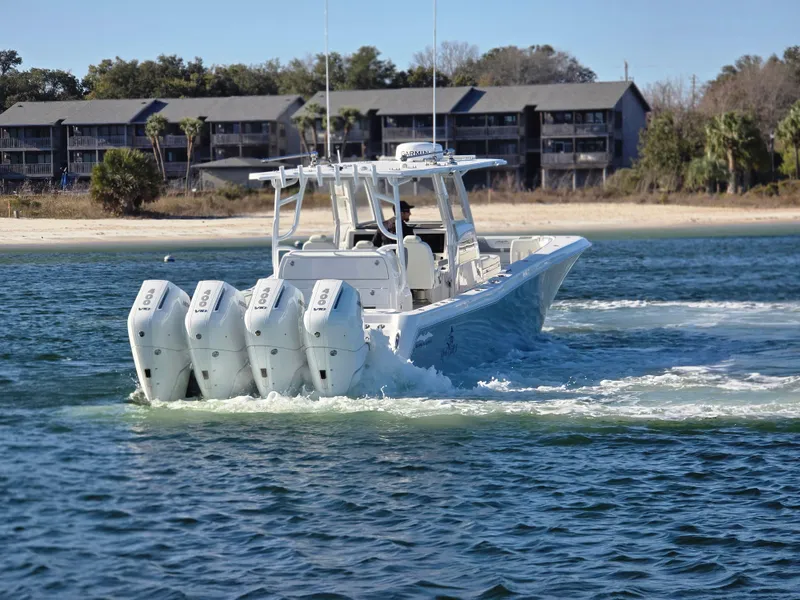 Slide: The Image of 2024 Invincible 43 Open Fisherman boat with four engines cruising near a sandy shoreline. - 21