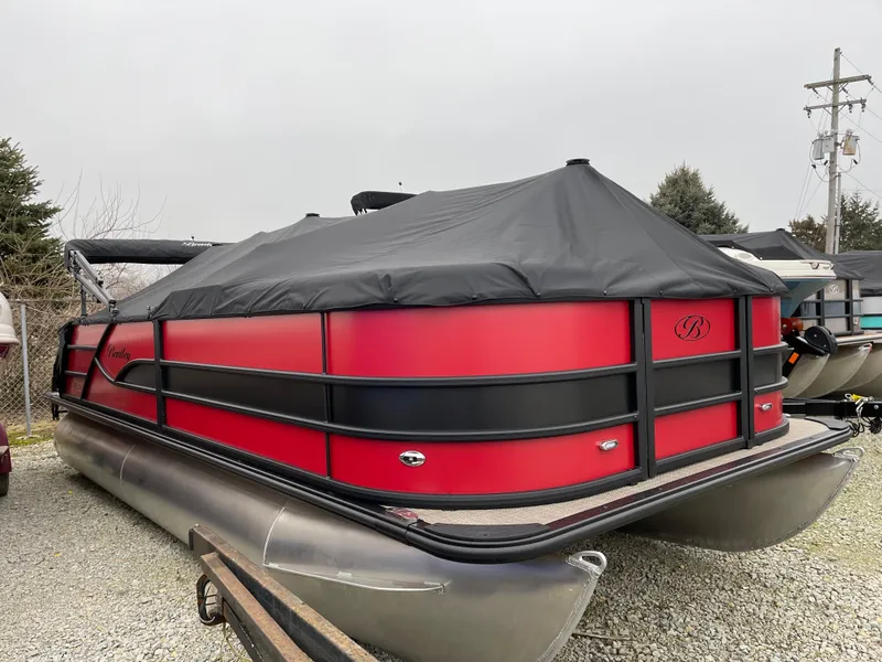 Slide: The Image of 2025 Bentley Pontoons Legacy 200 Swingback, red and black, covered, parked on gravel. - 2