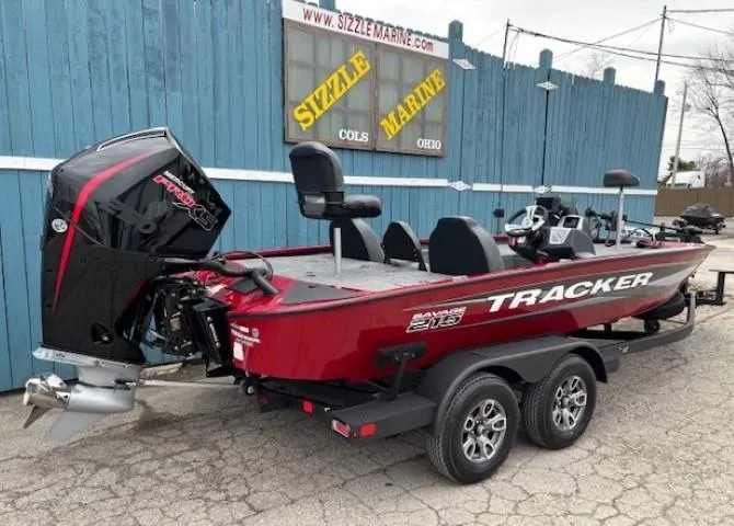 Slide: The Image of 2025 Tracker Savage 215 boat in red, parked on a trailer near a blue building. - 2