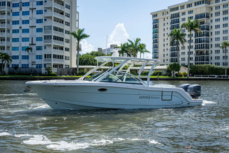 Slide: The Image of 2019 Robalo R317 Dual Console boat cruising near waterfront buildings. - 25