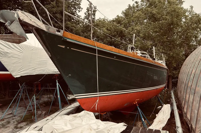 Slide: The Image of 1990 Bristol 47.7 sailboat on stands, green hull, red bottom, surrounded by trees. - 27