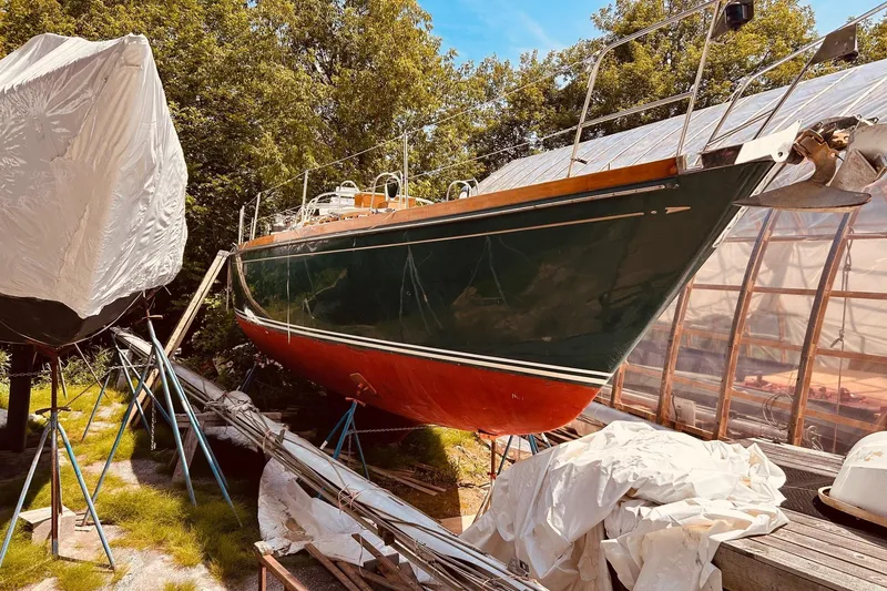 Slide: The Image of 1990 Bristol 47.7 sailboat on stands, surrounded by trees and covered structures. - 28