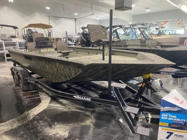 The Image of 2025 SeaArk Shadow 20 boat on trailer in showroom, camo design, well-lit environment. - 0