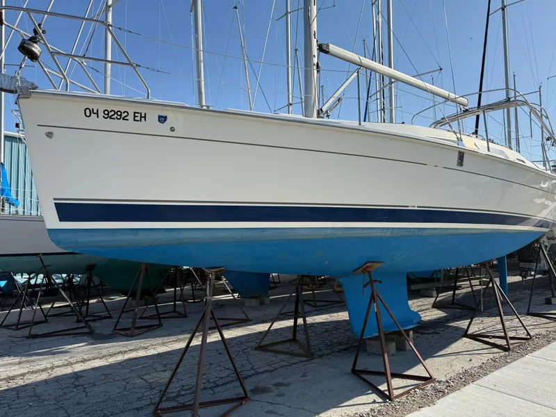 Slide: The Image of 2007 Hunter 33 sailboat on stands, white hull with blue stripe, in a boatyard. - 37