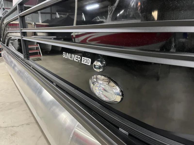 Slide: The Image of 2025 Harris Sunliner 230 pontoon boat, sleek black exterior detail in a showroom. - 9