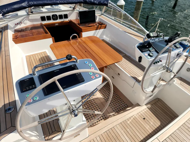 Slide: The Image of 2023 Hallberg-Rassy 57 yacht cockpit with dual steering wheels and wooden table. - 49