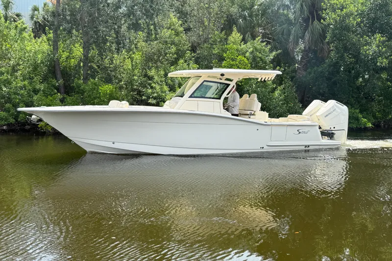 The Image of 2025 Scout 305 LXF boat cruising on a calm river surrounded by lush greenery. - 0