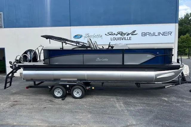 Slide: The Image of 2025 Barletta C22QC pontoon boat on trailer, parked outside dealership. - 2