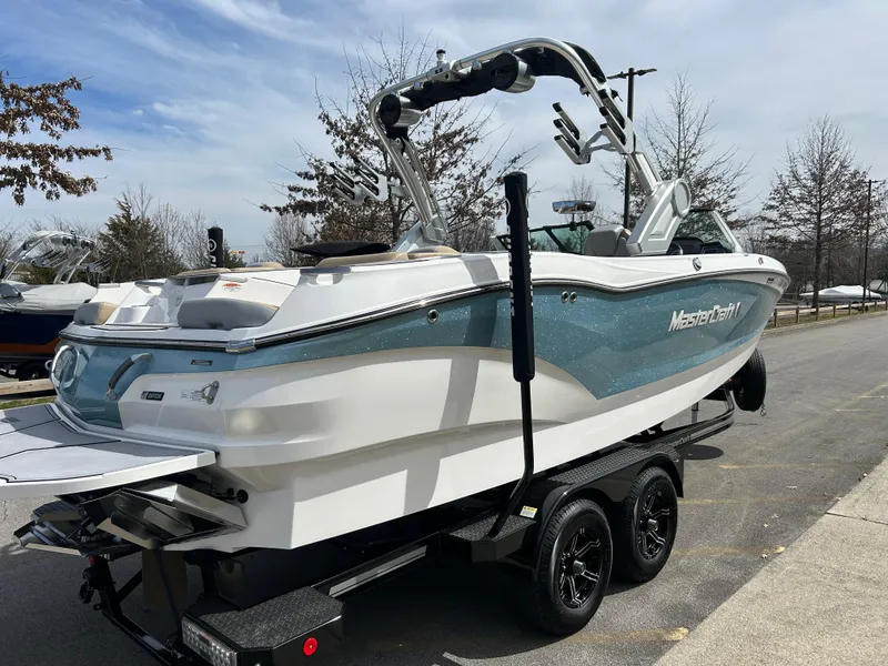 Slide: The Image of 2023 MasterCraft X24 boat on trailer, parked outdoors, side view. - 2