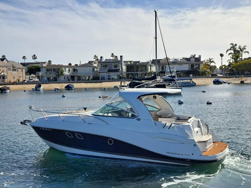 The Image of 2013 Rinker 310 Express Cruiser on calm water near coastal homes. - 0