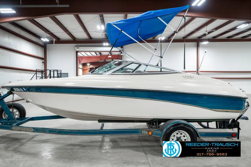Slide: The Image of 1995 Crownline 182 BR boat with blue canopy on trailer in warehouse. - 11