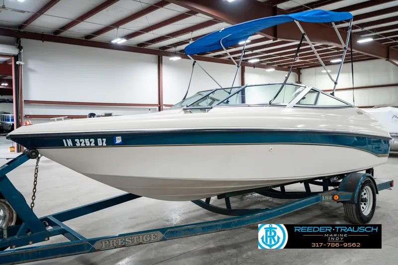 Slide: The Image of 1995 Crownline 182 BR boat on trailer with blue canopy in indoor storage. - 3