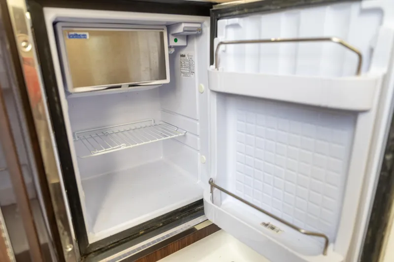 Slide: The Image of Open refrigerator inside 2023 Edgewater 370CC boat, showcasing storage space and shelving. - 16