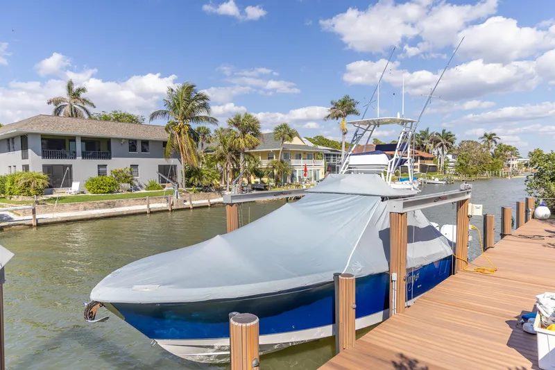 Slide: The Image of 2023 Edgewater 370CC boat docked, covered, with palm trees and waterfront homes in the background. - 41