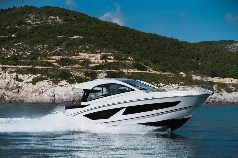 Slide: The Image of 2025 Beneteau 32 Gran Turismo cruising on water near rocky coastline. - 2