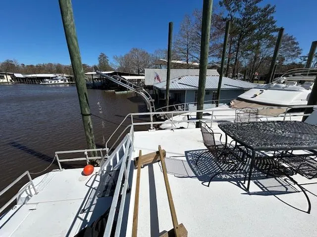 Slide: The Image of Houseboat deck with metal furniture, docked by a river, surrounded by trees and clear blue sky. - 49
