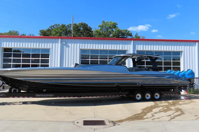 The Image of 2022 MTI 50v boat on trailer, parked outside a garage under a clear blue sky. - 0