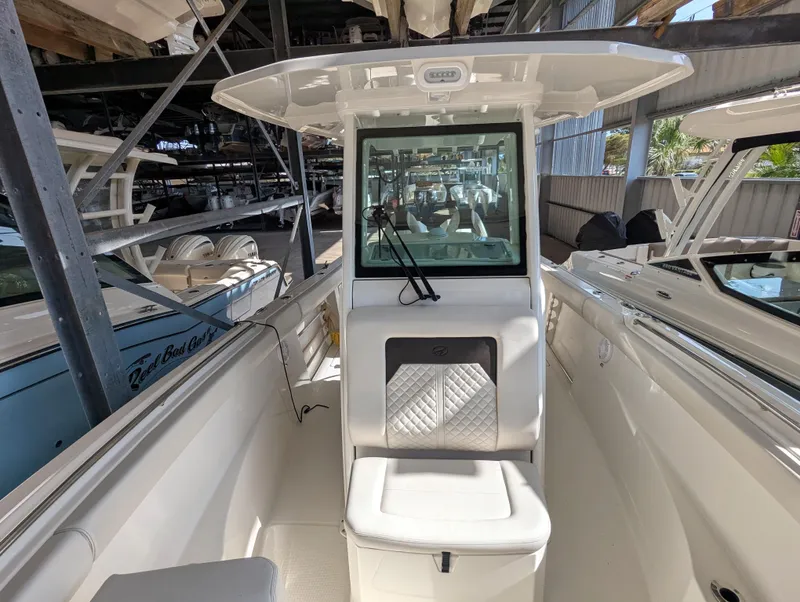 Slide: The Image of 2023 Sailfish 272 CC boat interior with seating and windshield in a marina setting. - 13