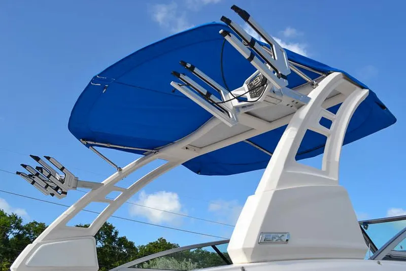 Slide: The Image of 2021 Chaparral 23 Surf boat with blue canopy and wakeboard tower against clear sky. - 25