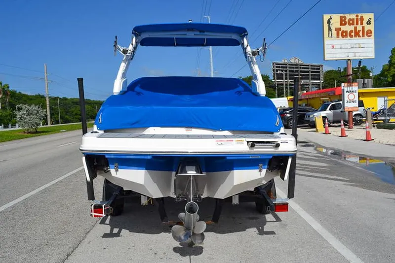 Slide: The Image of 2021 Chaparral 23 Surf boat with blue cover, parked near a bait and tackle shop. - 5