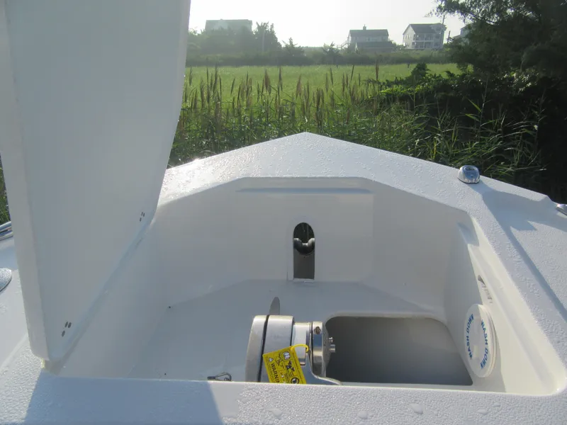 Slide: The Image of 2025 Parker 2900 Center Console boat anchor compartment with open hatch, grassy background. - 18