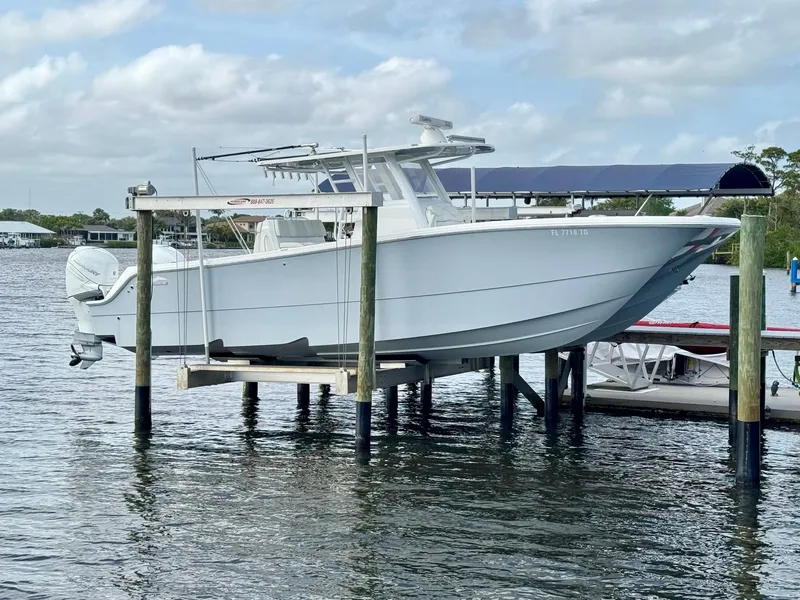 Slide: The Image of 2022 Invincible 33 Catamaran on lift, docked by calm waters under a cloudy sky. - 1