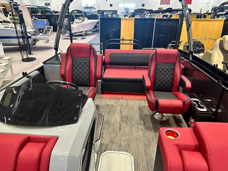 Slide: The Image of 2024 Godfrey AquaPatio 235 SFLC interior with red and black seating at a boat show. - 6
