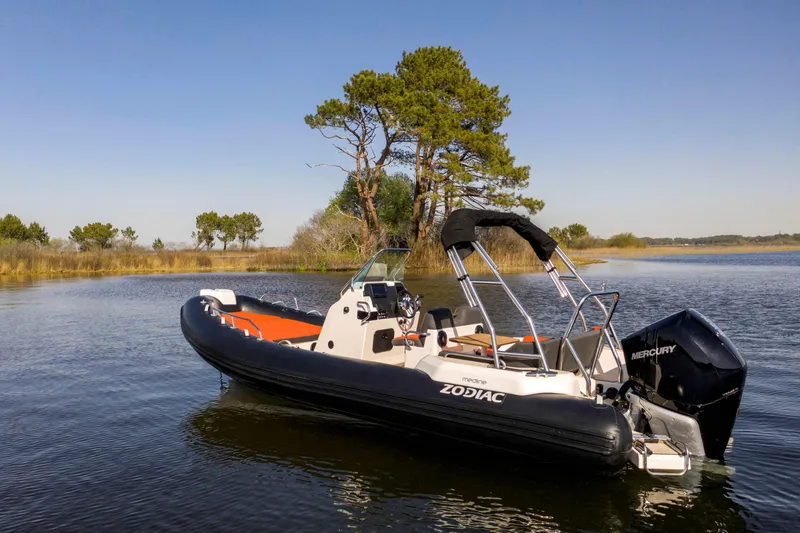 Slide: The Image of 2025 Zodiac Medline 6.8 boat on calm water, surrounded by trees under clear blue sky. - 14