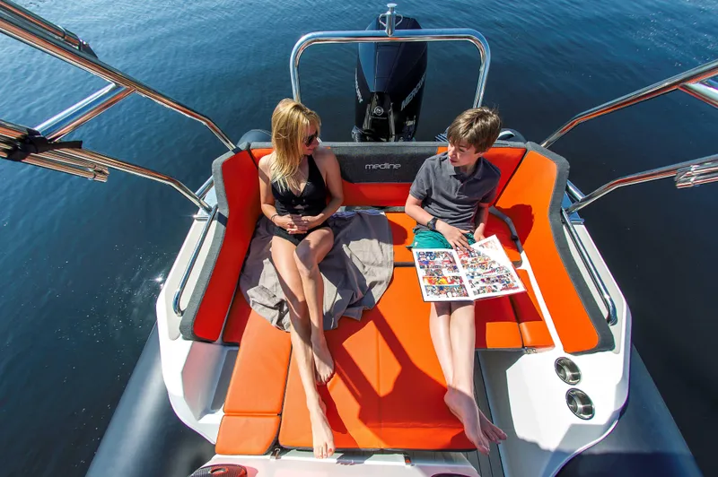 Slide: The Image of Two people relaxing on a 2025 Zodiac Medline 6.8 boat with orange seating. - 7