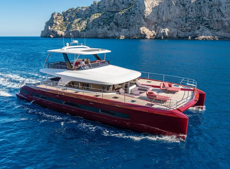 Slide: The Image of Luxurious 2025 Lagoon SIXTY 7 yacht cruising in clear blue waters near rocky cliffs. - 0