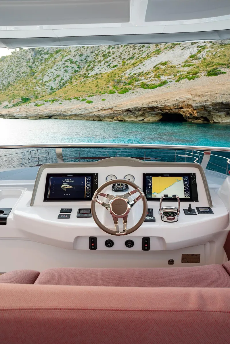 Slide: The Image of 2025 Lagoon SIXTY 7 yacht helm with dual screens, steering wheel, and scenic ocean view. - 10