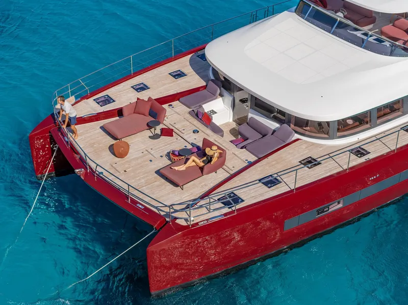 Slide: The Image of 2025 Lagoon SIXTY 7 yacht with red exterior, spacious deck, and people relaxing on turquoise water. - 4