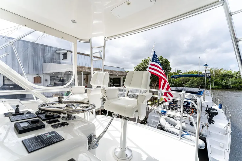 Slide: The Image of 2003 Bertram 570 Moppie yacht helm with American flag, docked near lush greenery. - 16