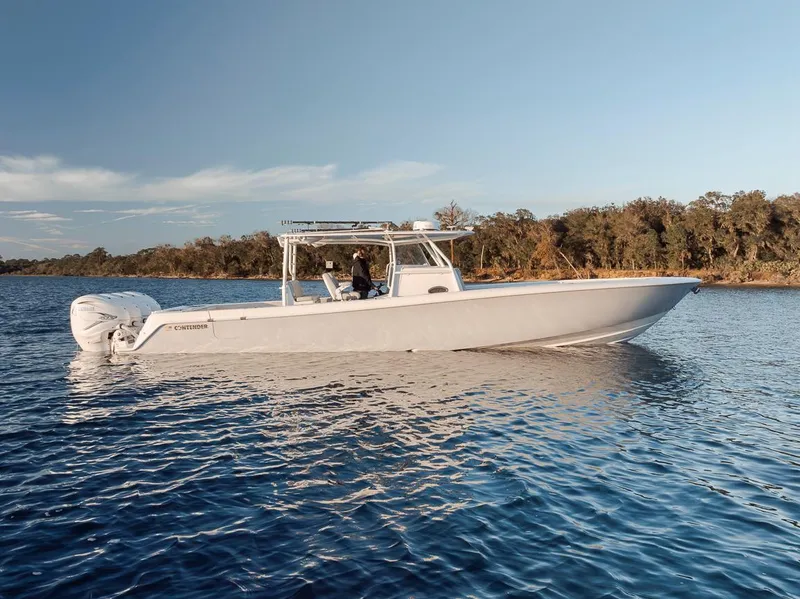 Slide: The Image of 2021 Contender 44 ST boat on calm water, clear sky, and wooded shoreline. - 2