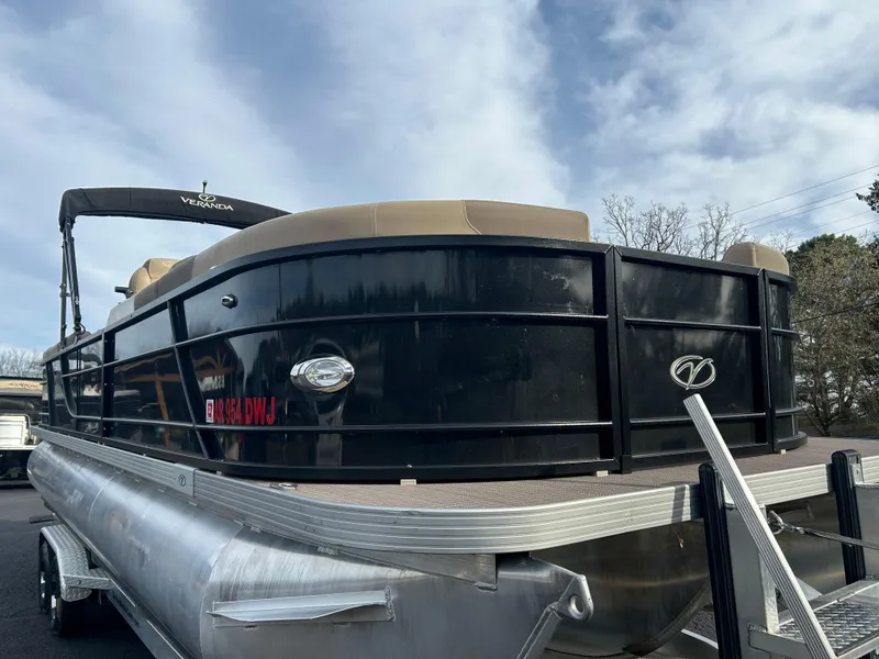 Slide: The Image of 2022 Veranda Relax VR25RC pontoon boat with black exterior, docked under a cloudy sky. - 2