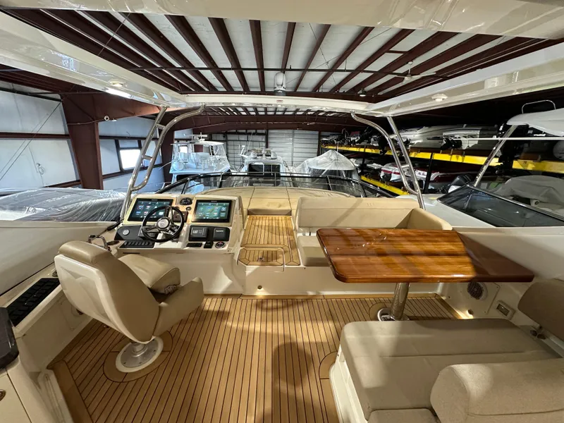 Slide: The Image of 2015 Sea Ray L650 Flybridge interior with helm, seating, and wooden table in a boat storage facility. - 4