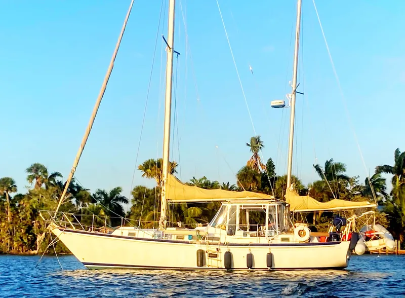 The Image of 1975 Whitby 42 Center Cockpit sailboat on water, surrounded by palm trees. - 0