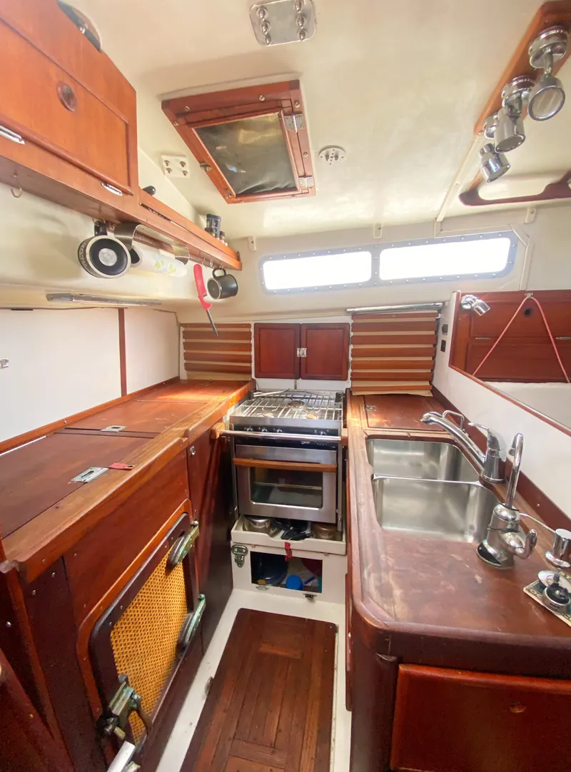 Slide: The Image of 1975 Whitby 42 Center Cockpit interior with wooden cabinetry and compact kitchen setup. - 12