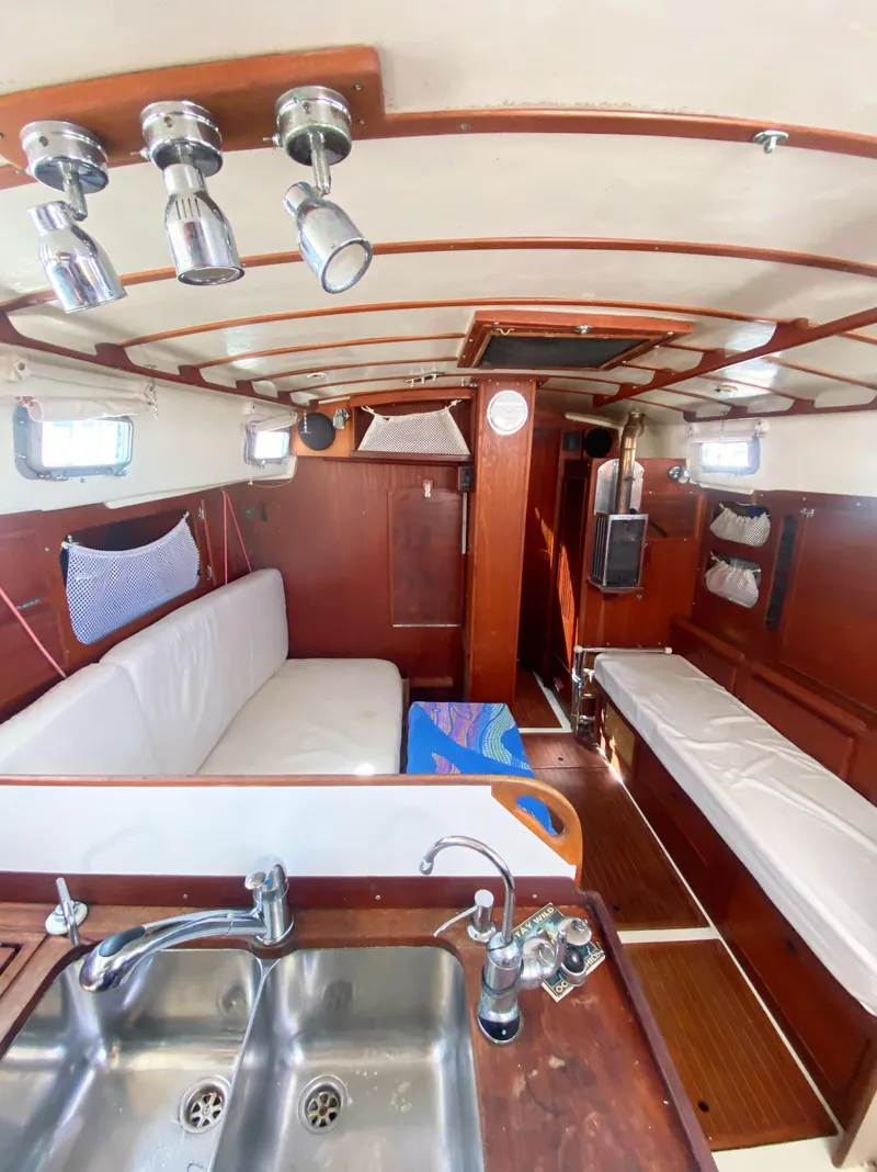 Slide: The Image of 1975 Whitby 42 Center Cockpit interior with wood finish, white seating, and stainless steel sink. - 17