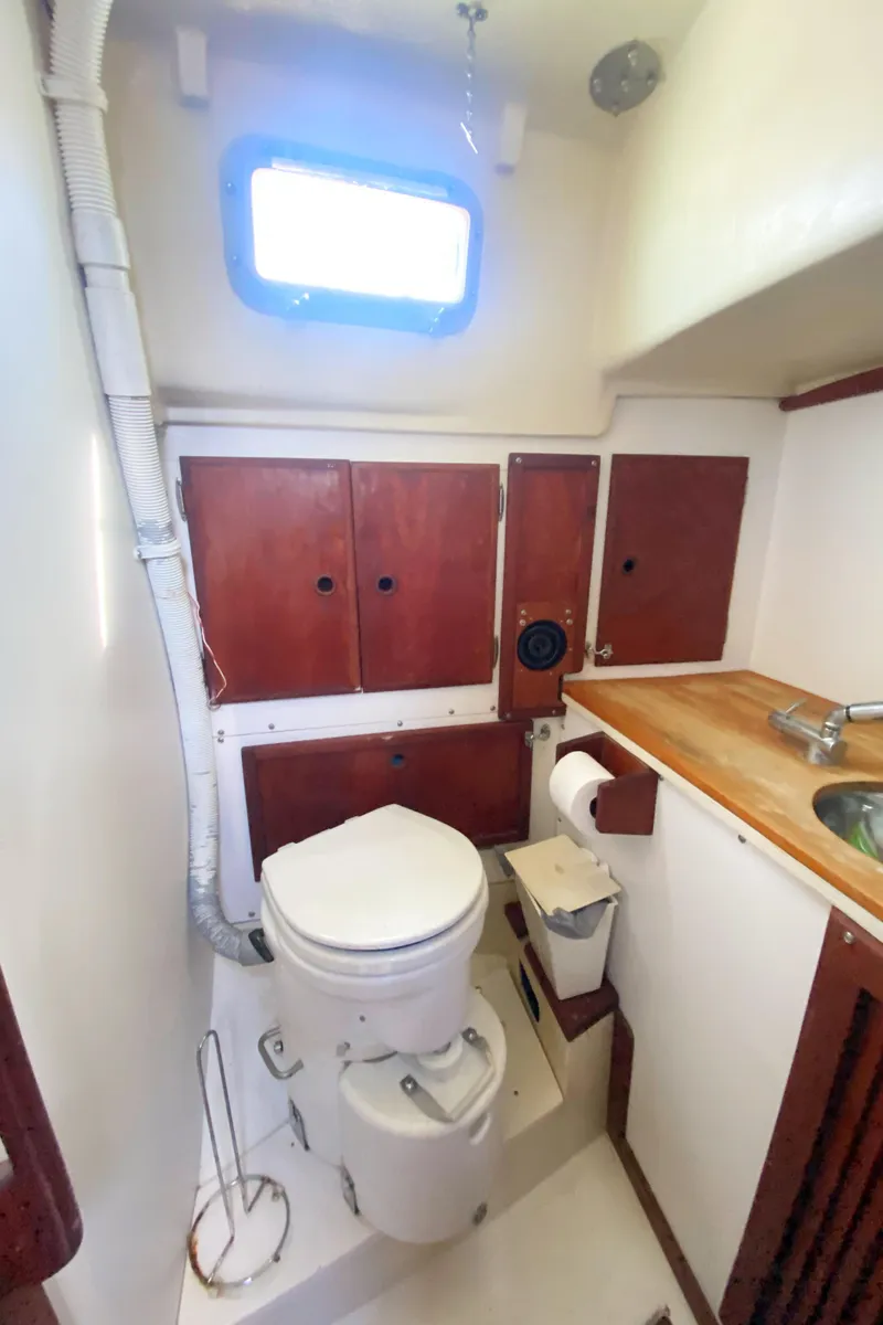 Slide: The Image of 1975 Whitby 42 Center Cockpit bathroom with wooden cabinets and a porthole window. - 35