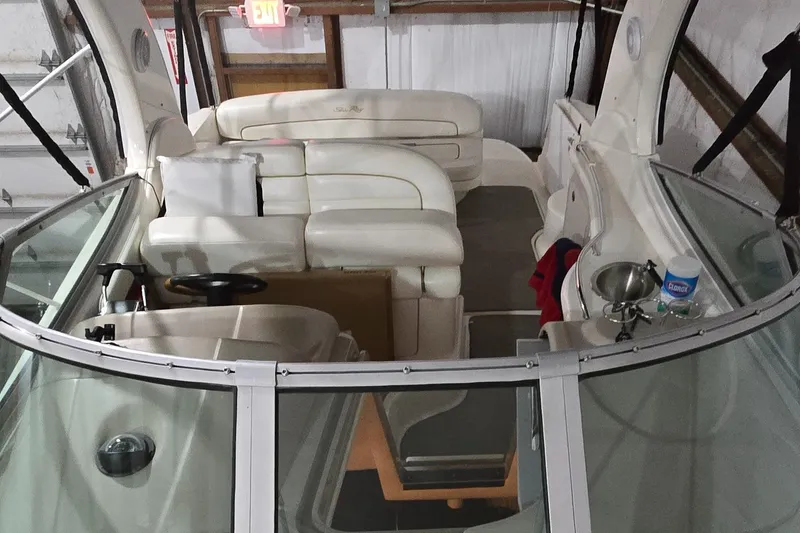 Slide: The Image of 2002 Sea Ray 300 Sundancer interior with white seating and helm, docked indoors. - 14