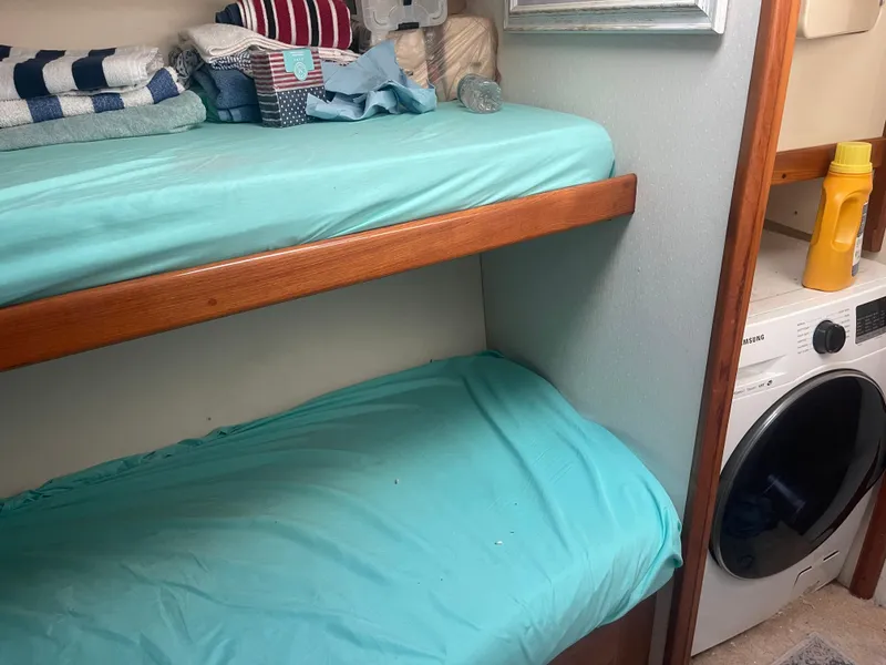 Slide: The Image of Bunk beds with teal sheets in a 1999 Viking 58 EB yacht cabin, adjacent to a washing machine. - 23
