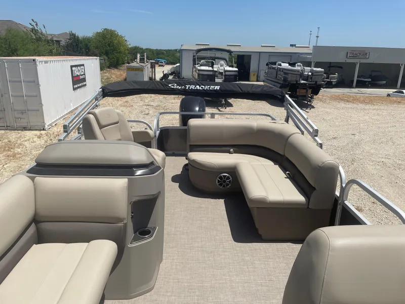 Slide: The Image of 2025 Sun Tracker Party Barge 18 DLX pontoon boat with beige seating, parked outdoors. - 7