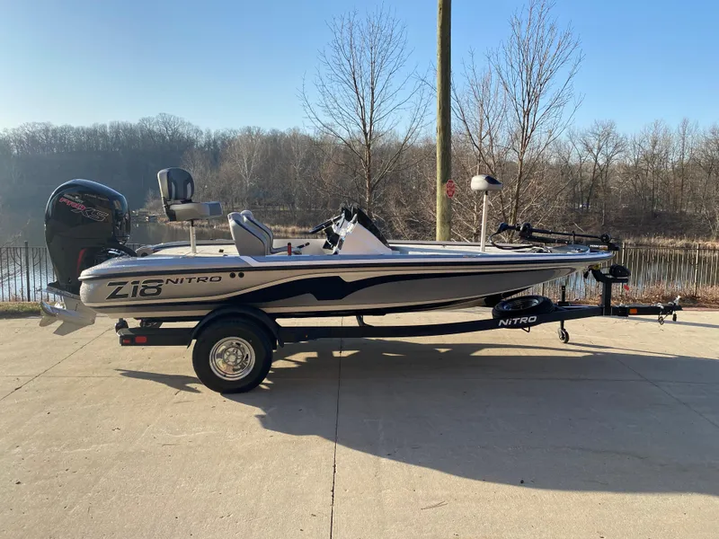 Slide: The Image of 2025 Nitro Z18 boat on trailer, parked near a lake with trees in the background. - 0