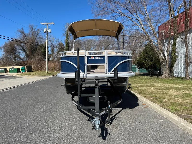Slide: The Image of 2025 Sun Tracker Fishin' Barge 20 DLX pontoon boat on trailer, parked on a sunny street. - 2
