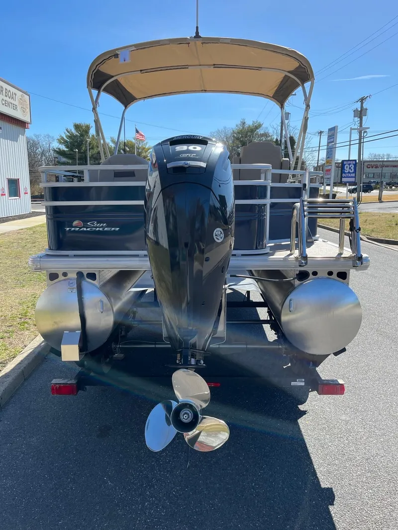 Slide: The Image of 2025 Sun Tracker Fishin' Barge 20 DLX pontoon boat, rear view with motor, parked outdoors. - 5