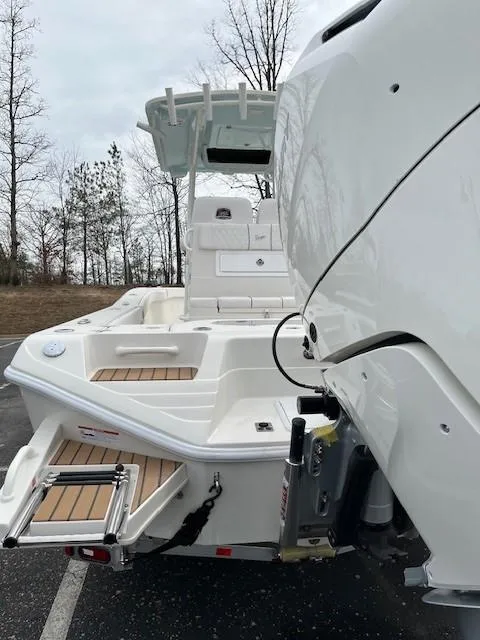 Slide: The Image of 2025 Ranger 2600 Bay boat, rear view, showcasing deck and motor in a wooded area. - 2