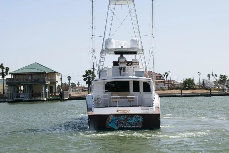 Slide: The Image of 1998 Huckins 70 Sportfish Convertible yacht cruising near coastal homes. - 12